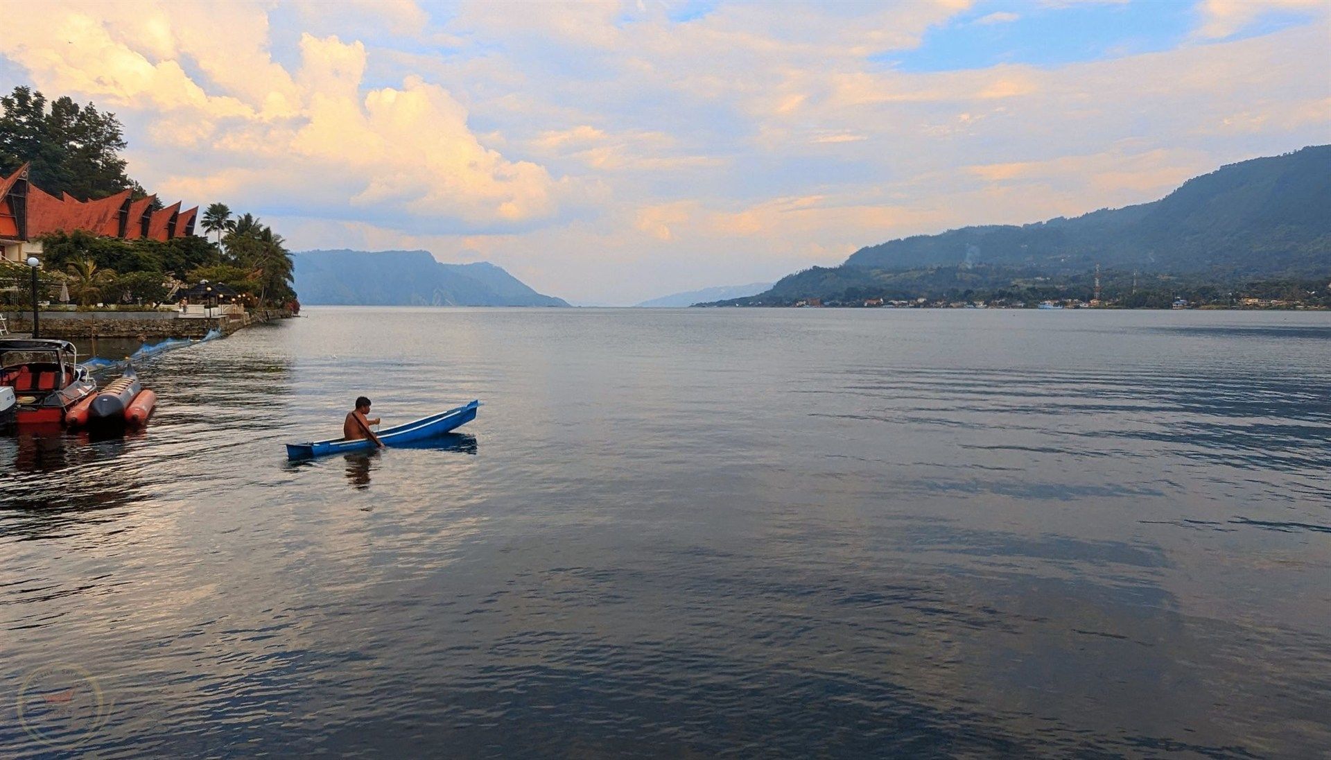 A man is paddling a kayak on a lake with mountains in the background.