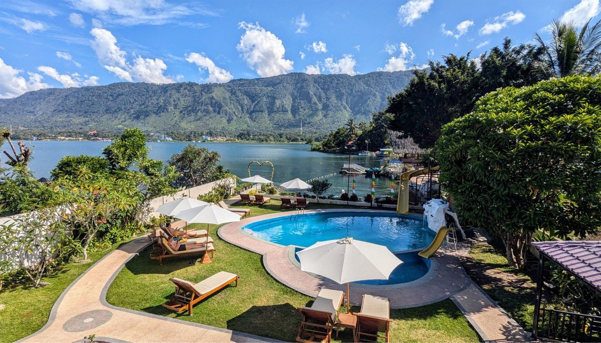 A large swimming pool surrounded by chairs and umbrellas next to a lake.