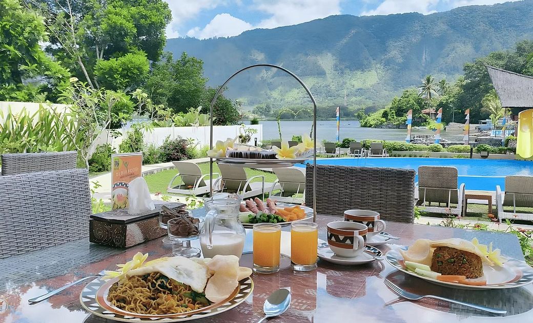 A table topped with plates of food and drinks with a pool in the background.