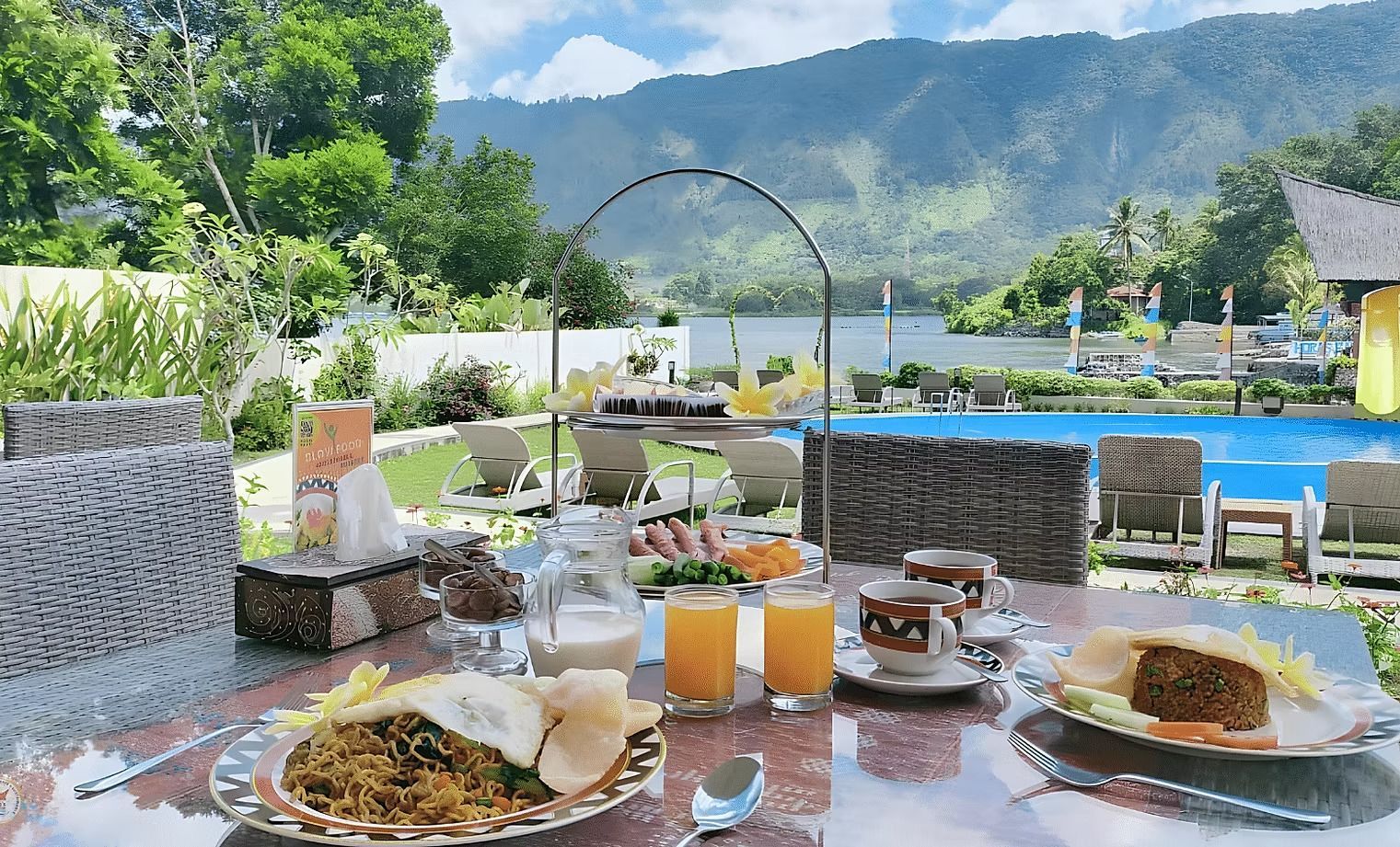 A table topped with plates of food and drinks with a pool in the background.