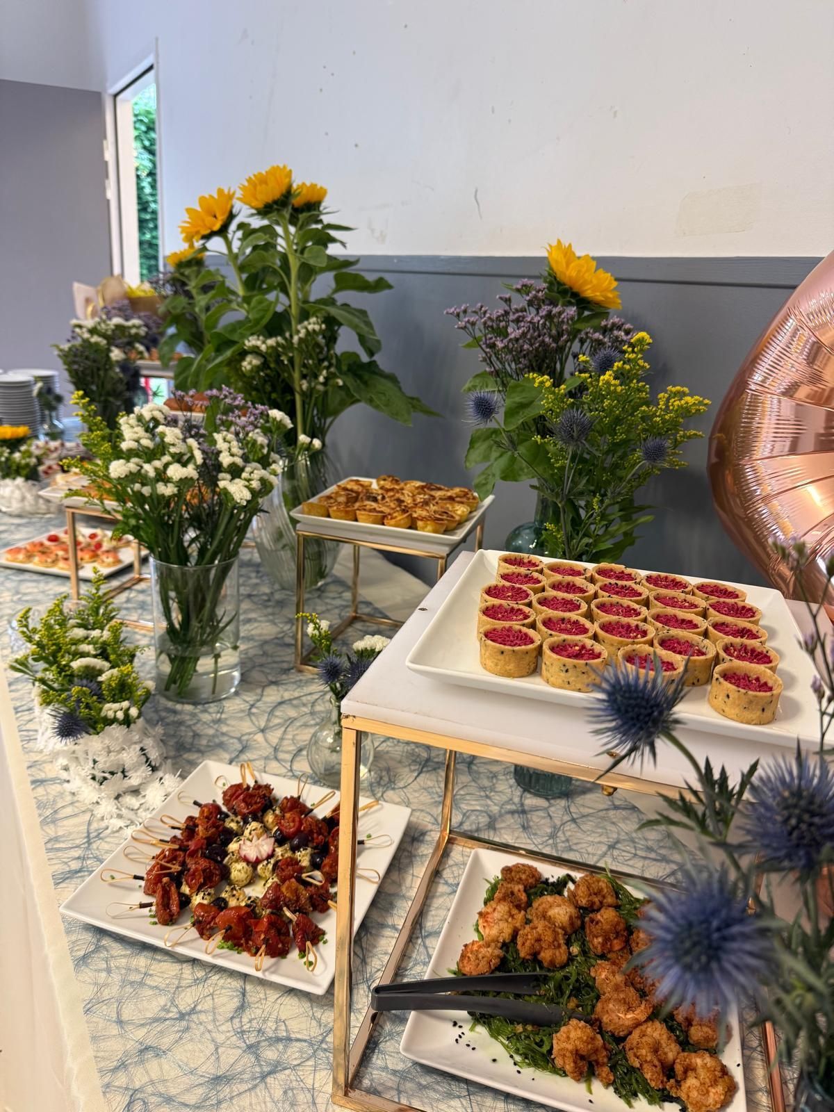 Un buffet avec divers amuse-gueules, décoré de fleurs colorées. Les plats comprennent des compositions sucrés salés.