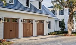 A white house with brown garage doors and a tree in front of it.