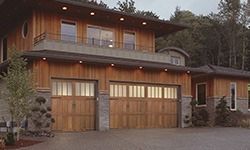 A large wooden house with two garage doors and a balcony.