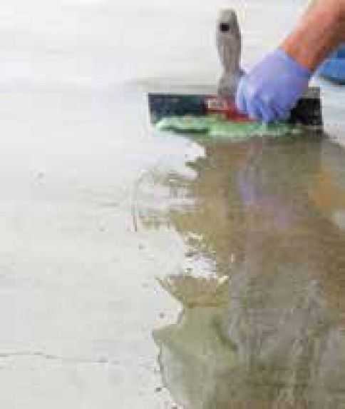 A person is using a spatula to spread a liquid on a concrete floor.