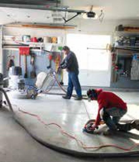 Two men are working on a concrete floor in a garage.