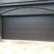 A black garage door is on the side of a brick building.