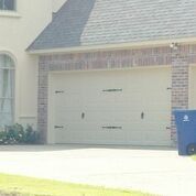 A blue trash can is parked in front of a white garage door.