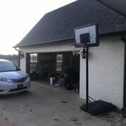 A car is parked in front of a garage with a basketball hoop.