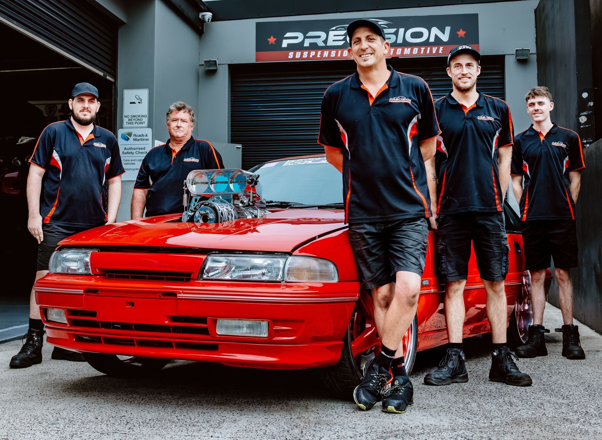 Five men in black uniforms pose with a red drag car in a garage — Mechanic in Wollongong, NSW