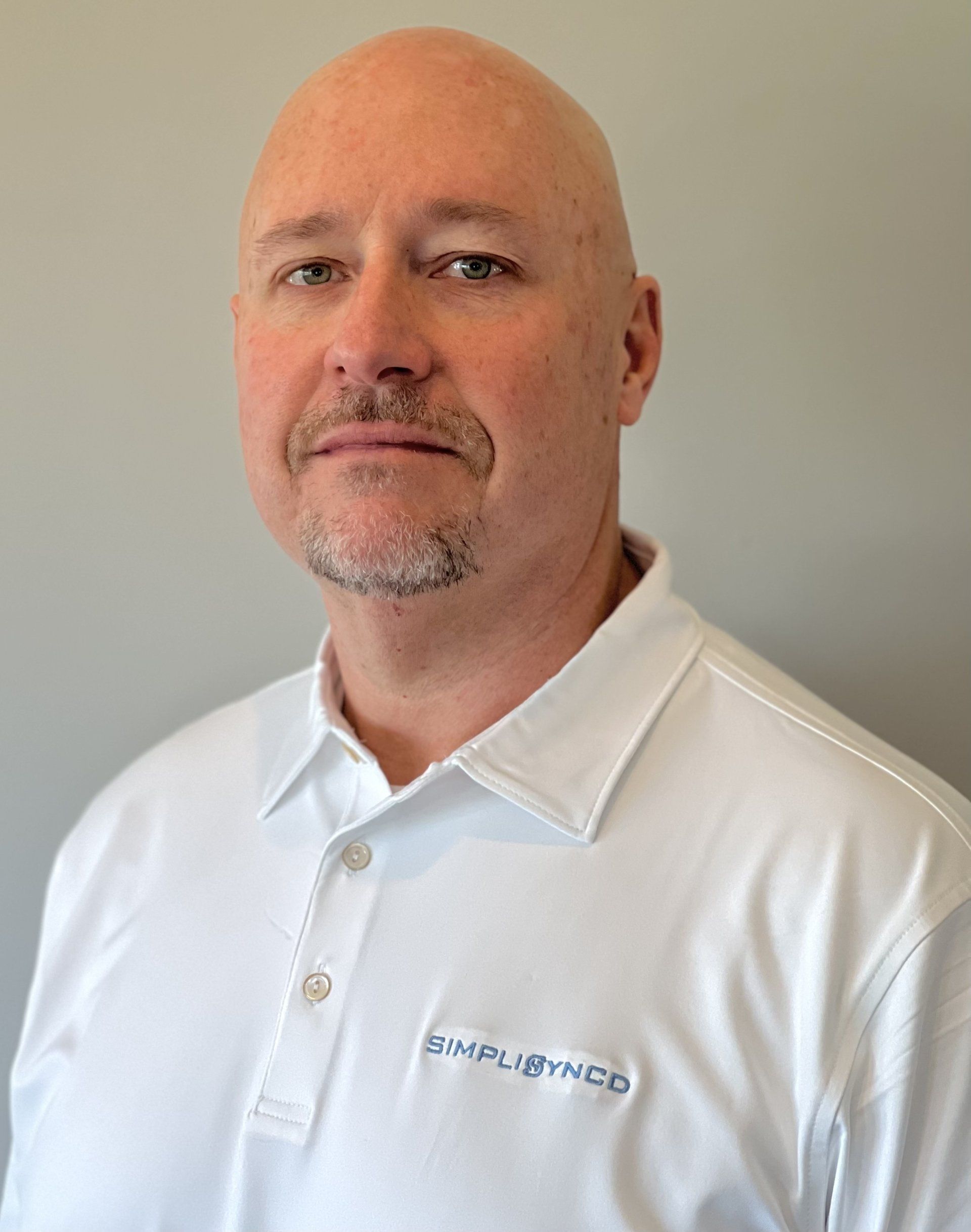 A man with a beard is wearing a white polo shirt.