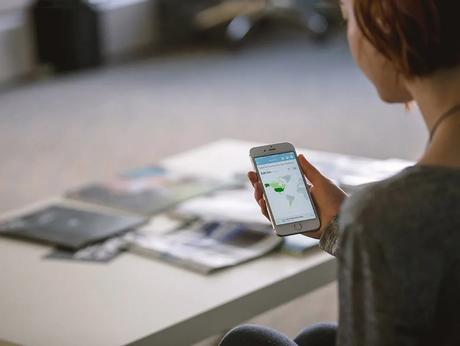 A woman is sitting at a table holding a cell phone in her hand.