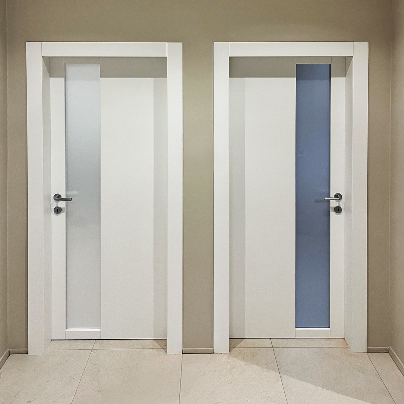 Due porte interne bianche con pannelli verticali in vetro, installate una accanto all'altra in un corridoio con pareti beige.