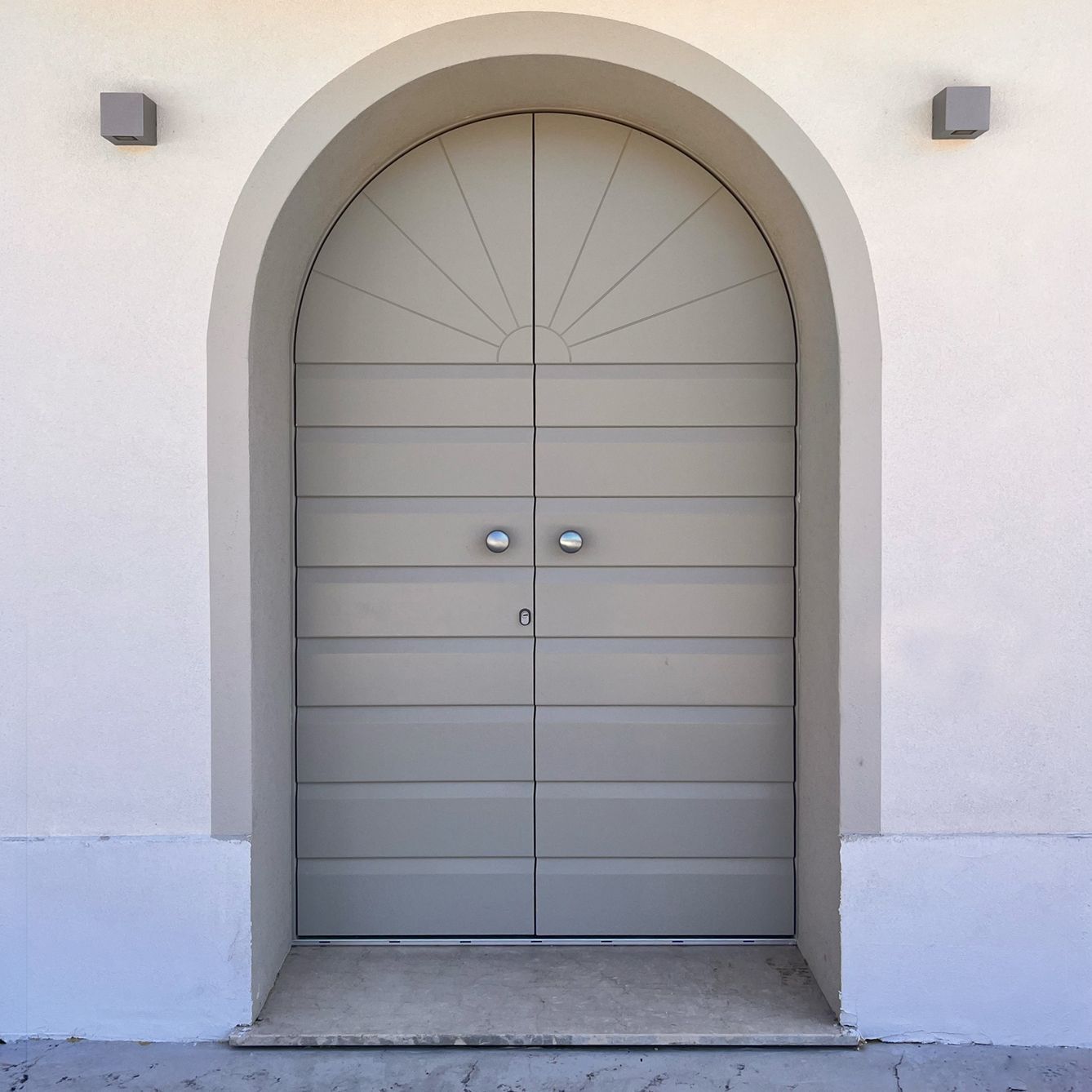 Una doppia porta ad arco grigio chiaro incastonata in una parete bianca