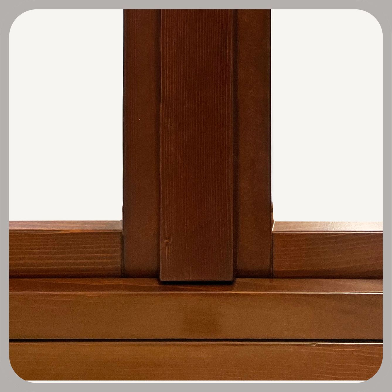 Vista ravvicinata degli incastri in legno tinto di un telaio di finestra, che mostra l'intersezione tra un montante verticale e un traverso.