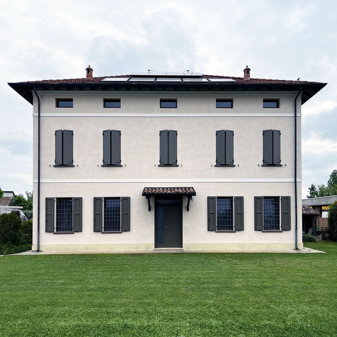 Una casa simmetrica a due piani, intonacata di rosa pallido, con persiane grigio scuro e ingresso centrale, situata su un prato verde.