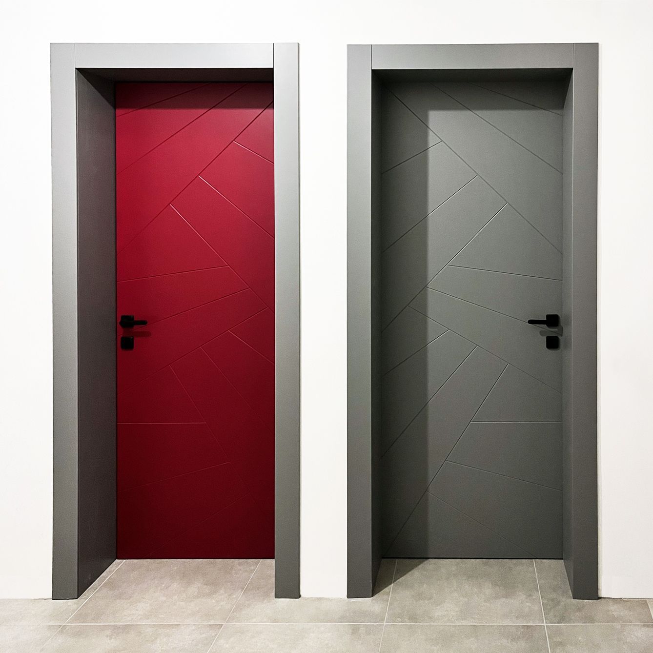 Due porte interne moderne con linee geometriche intagliate, una rossa e una grigia, incastonate in una parete bianca con cornici grigie.