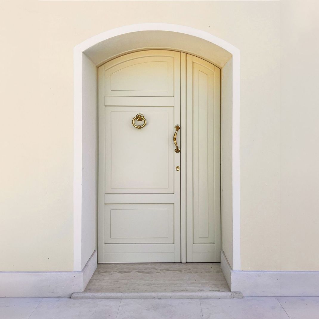Una porta di legno color crema con battente e maniglia dorati