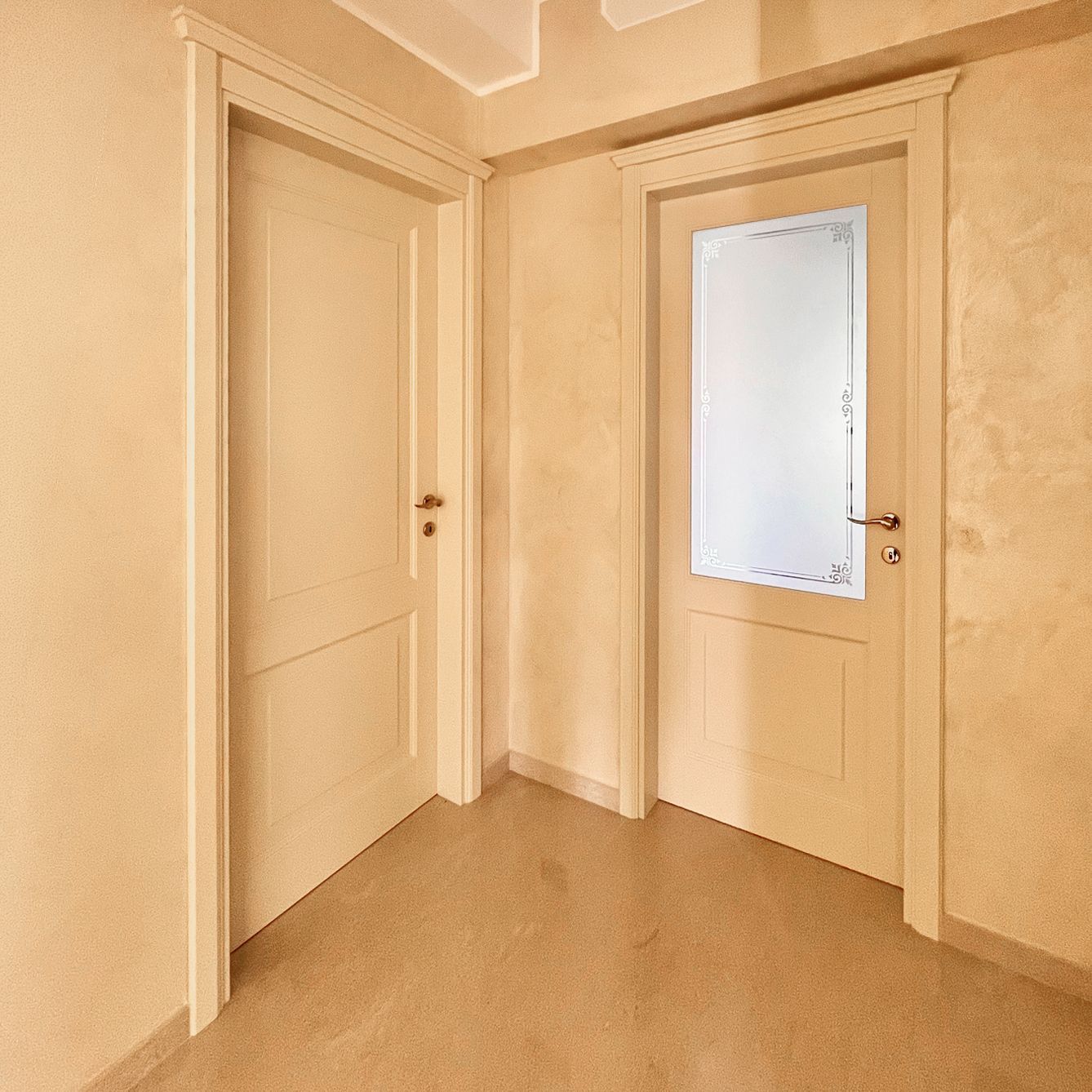 Un corridoio beige con due porte interne chiuse; una è piena, l'altra presenta un pannello di vetro rettangolare.