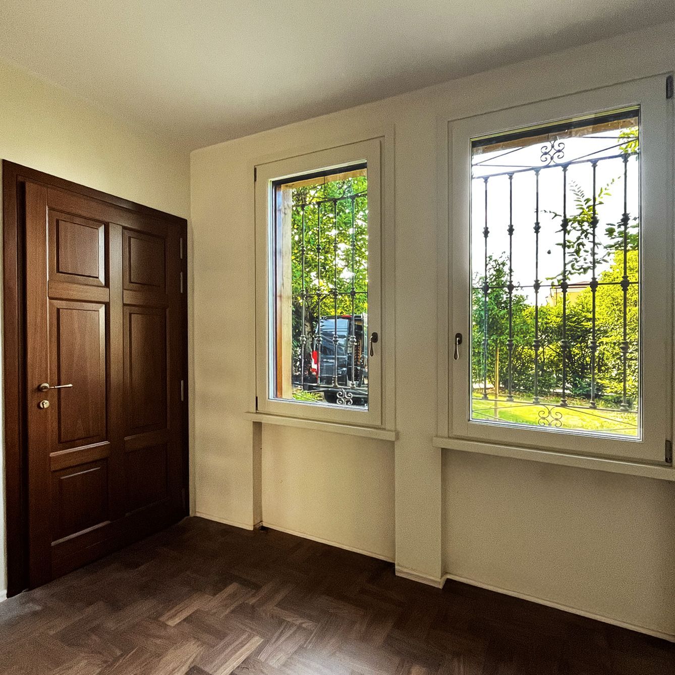 Due finestre con cornici marroni che si incontrano ad angolo, dotate di persiane avvolgibili a lamelle scure, parzialmente abbassate.