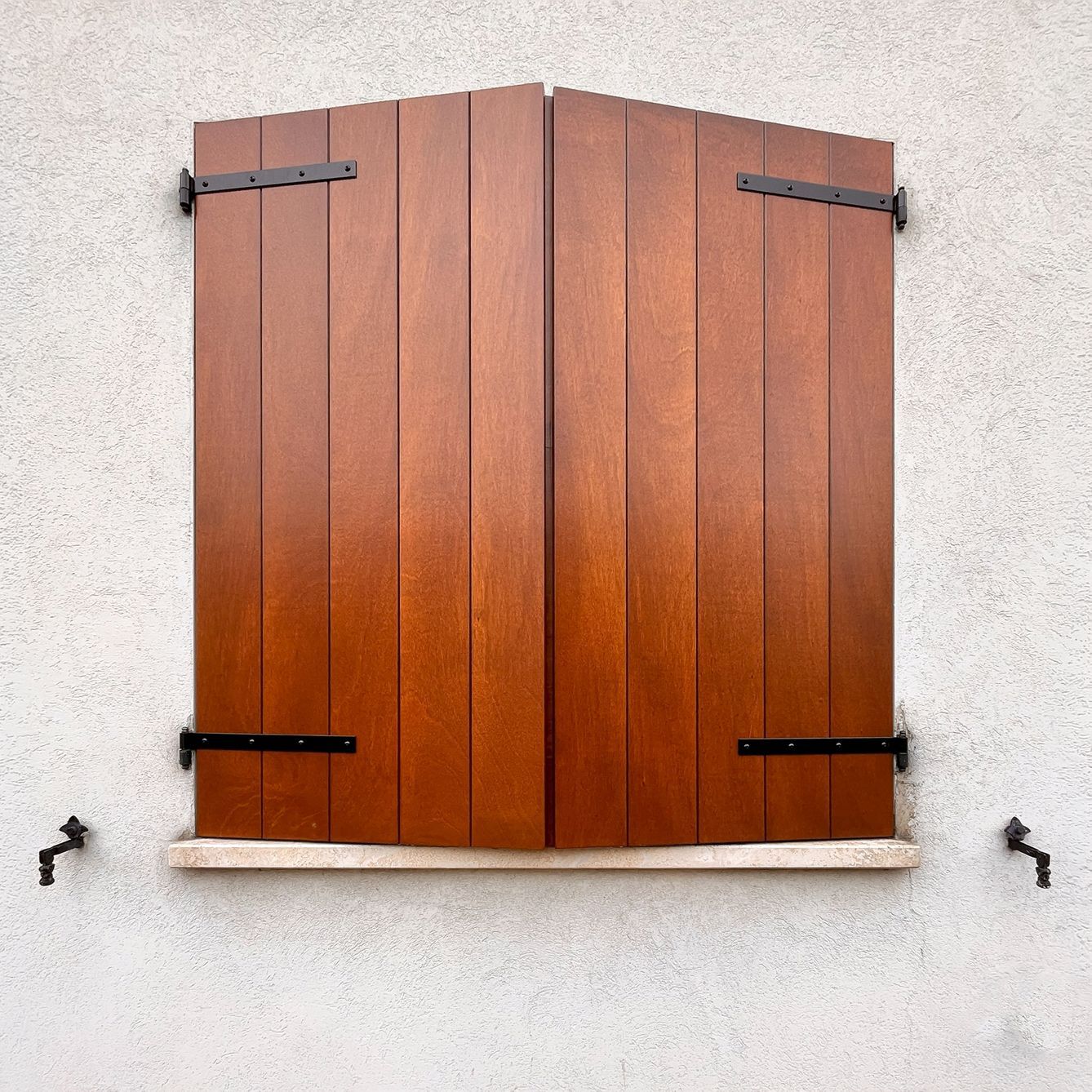 Una finestra rettangolare con persiane a pannelli grigio scuro si apre su entrambi i lati e una pesante gabbia di sicurezza in ferro con motivo a griglia.