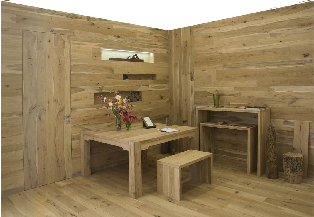 Una stanza con pareti e pavimento rivestiti in legno, arredata con un tavolo, una panca, una consolle e delle decorazioni a muro intagliate.