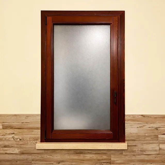 Una finestra rettangolare a vetro singolo con cornice in legno scuro e vetro satinato, incastonata in una parete color crema con battiscopa in legno.