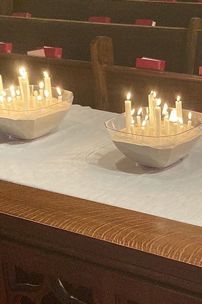 multiple lighted white candles in sand within square glass bowls