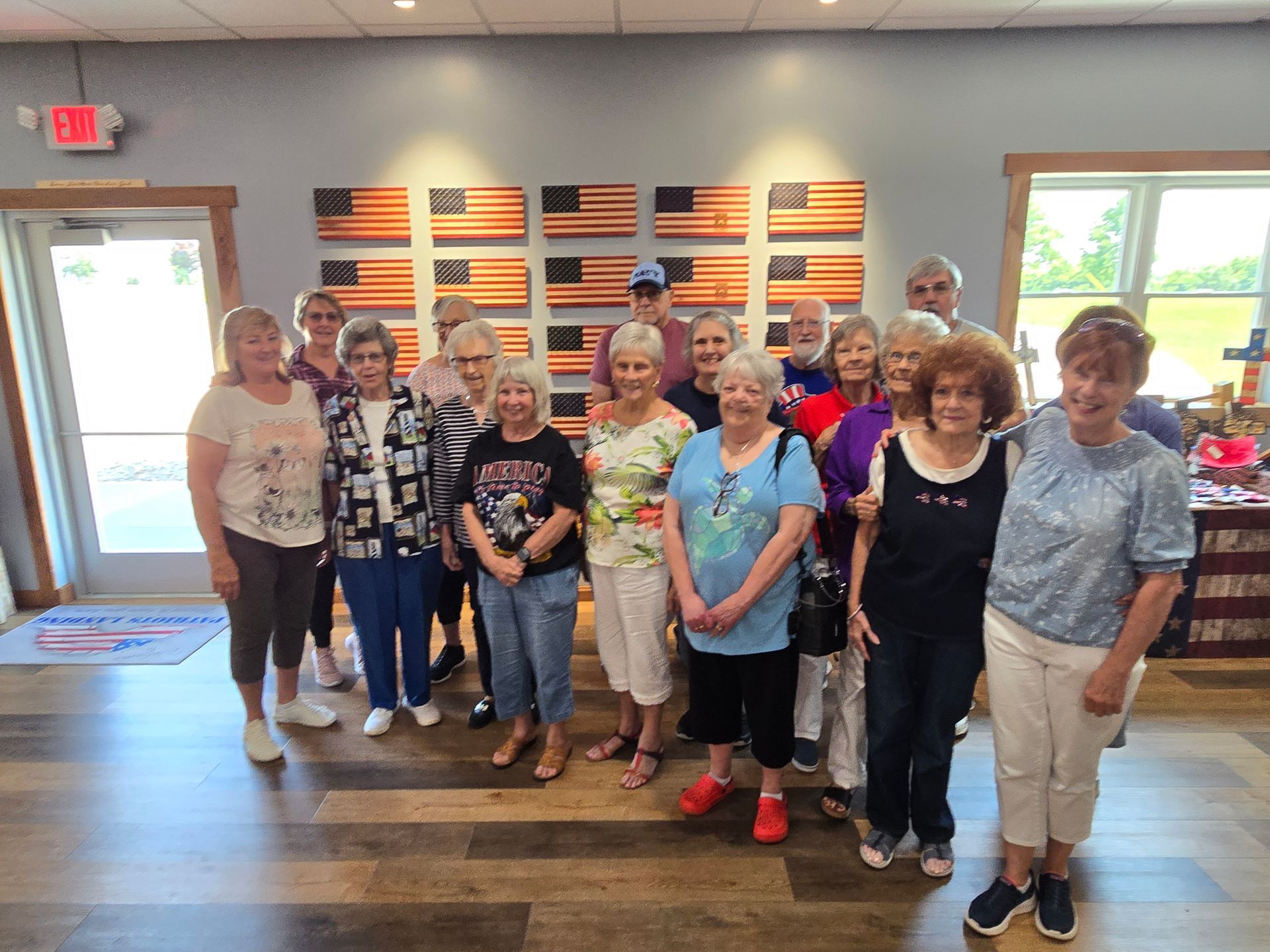 A group of senior adults pose inside a room with American flag art on the wall.