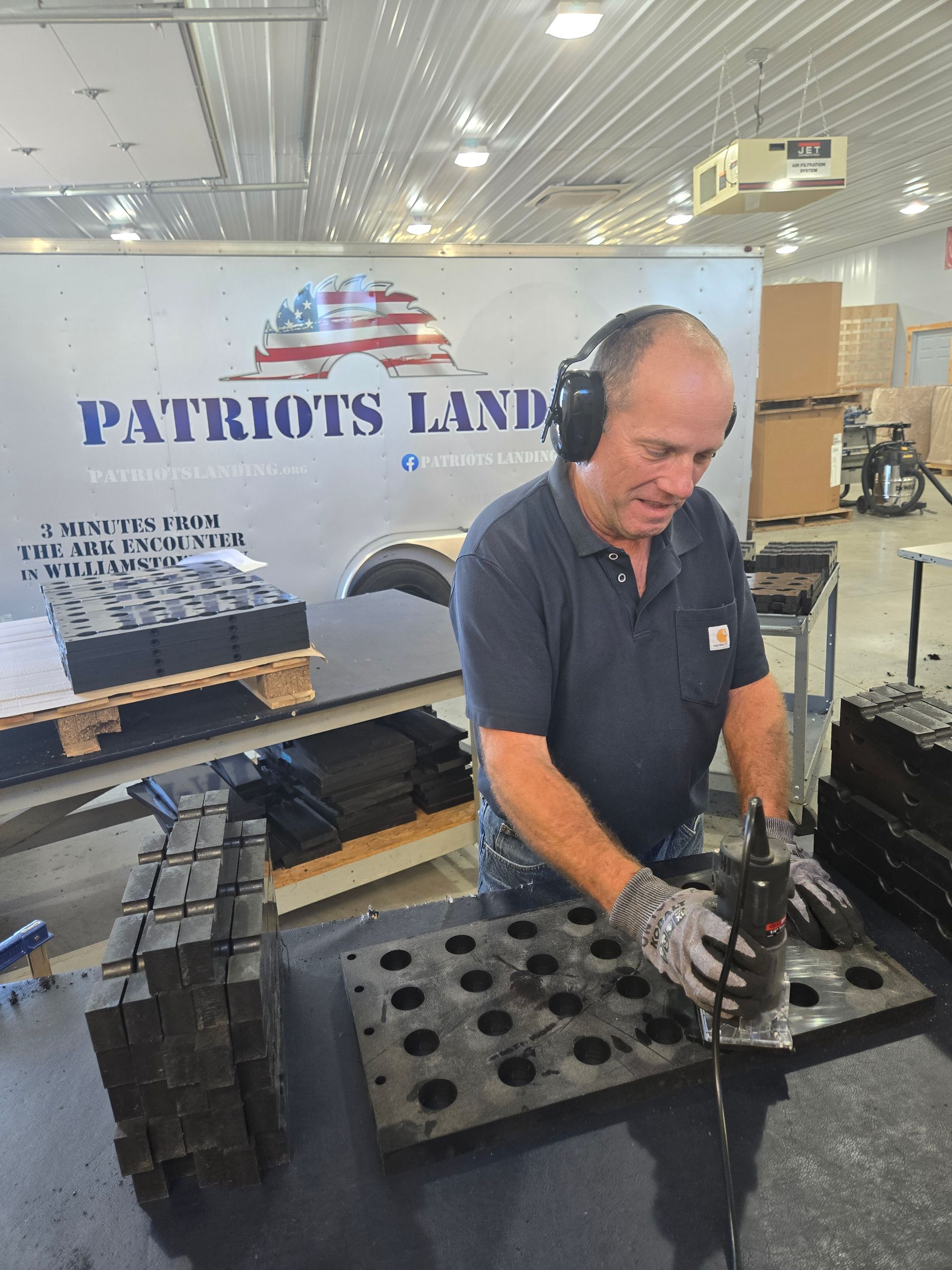 Man in warehouse wearing ear protection uses tool on a mold.
