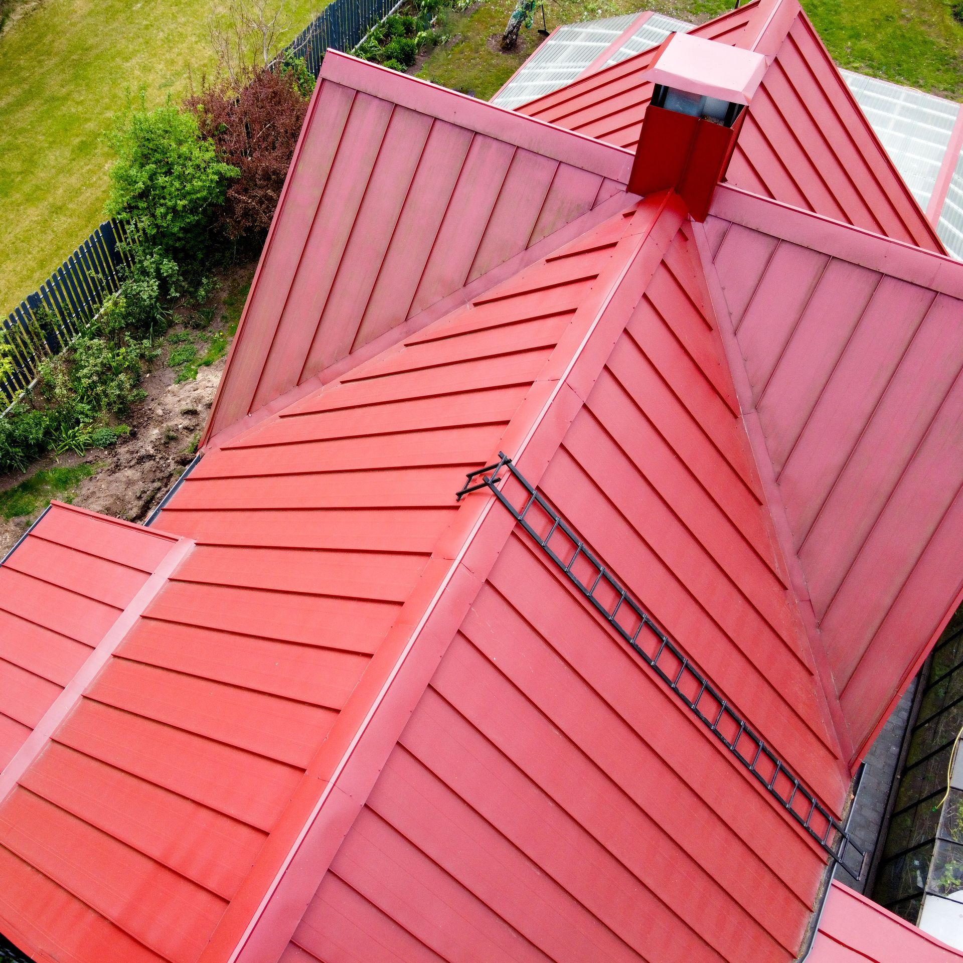 A worker holds a large, gray, corrugated metal roofing sheet with a crane in an outdoor setting.
