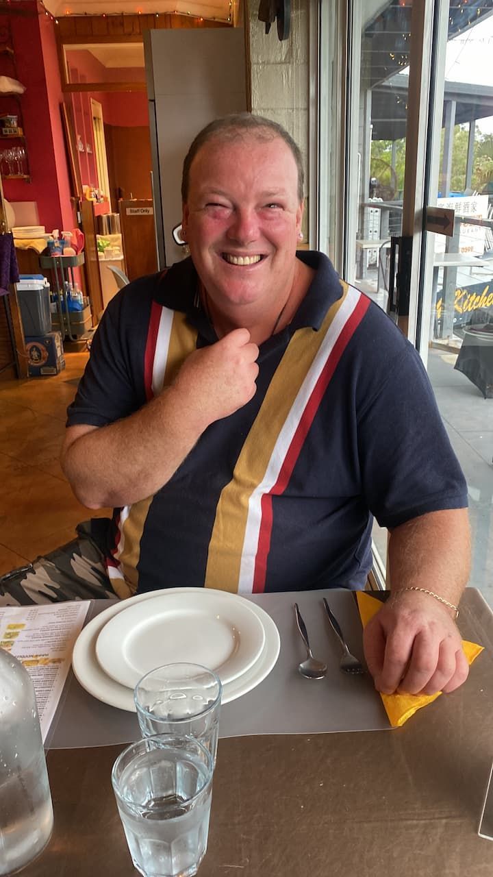 A Man is Smiling While Sitting at a Table With Plates and Glasses — Mentally Hooked in Robina, QLD