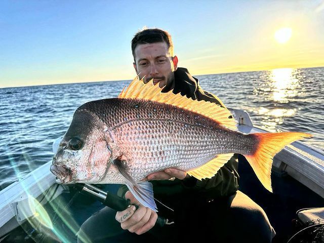 A Man is Holding a Large Fish on a Boat in the Ocean — Mentally Hooked in Robina, QLD