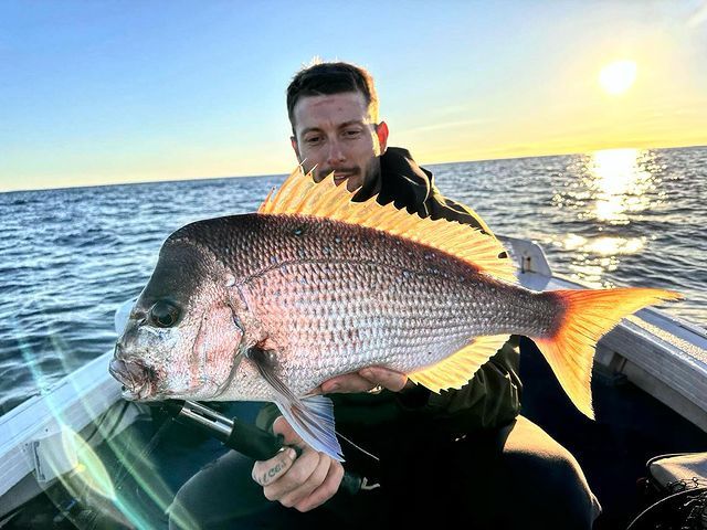 A Man is Sitting on a Boat Holding a Large Fish — Mentally Hooked in Robina, QLD