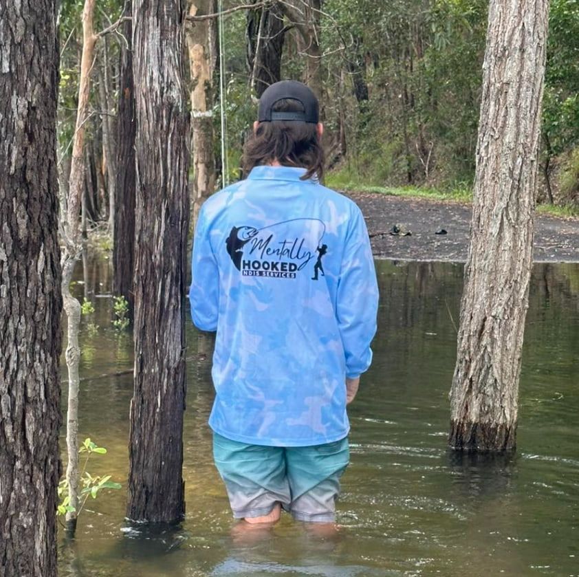 A Man in a Blue Shirt is Kneeling in the Water — Mentally Hooked in Robina, QLD