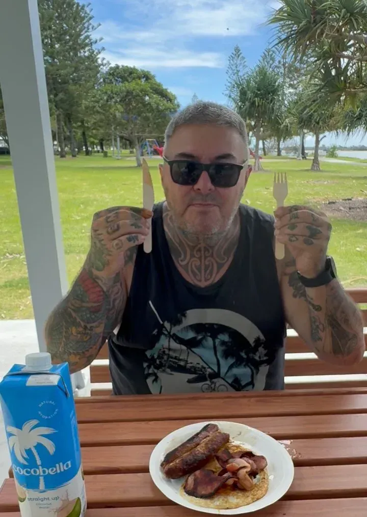 Man with tattoos holding cutlery over plate of food, seated outdoors under a gazebo — Mentally Hooked in Brisbane, QLD