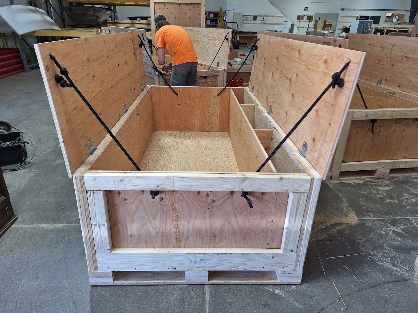 A wooden shipping crate with an open lid; a person works on the crate in a workshop.