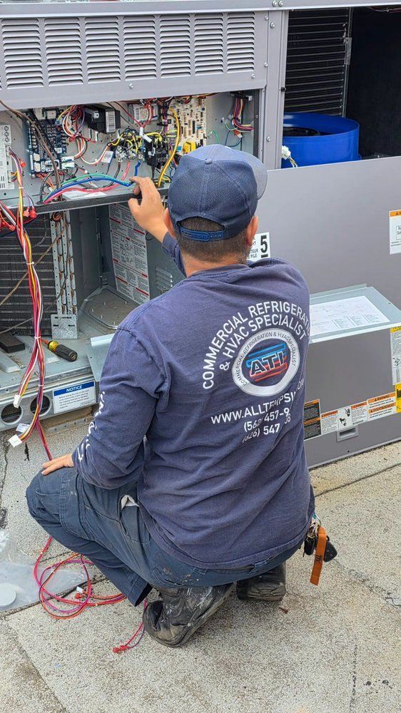 Technician kneeling at an open electrical panel, checking wiring on a utility unit outdoors.