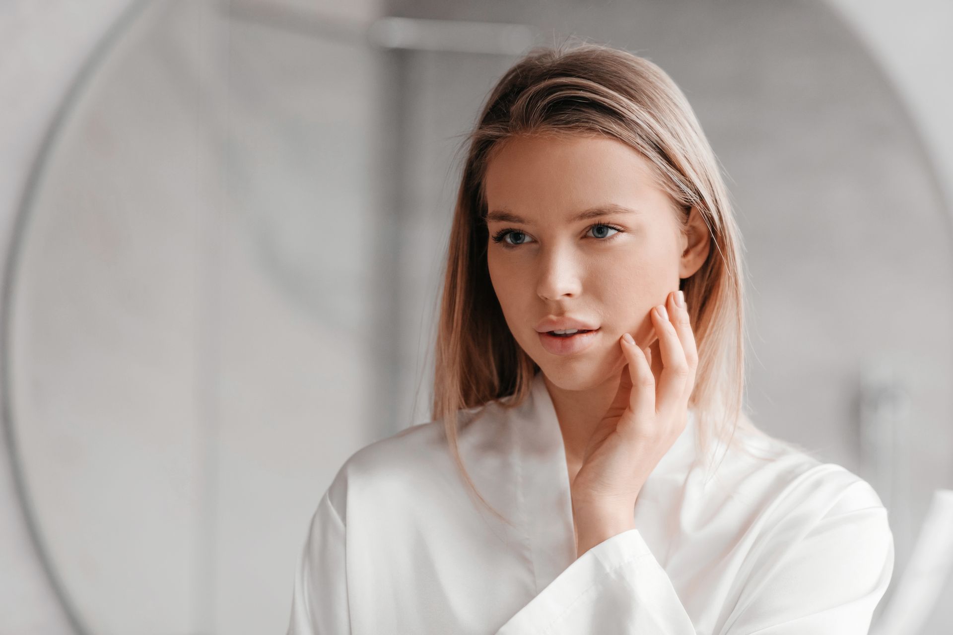 A woman is touching her face in front of a mirror.