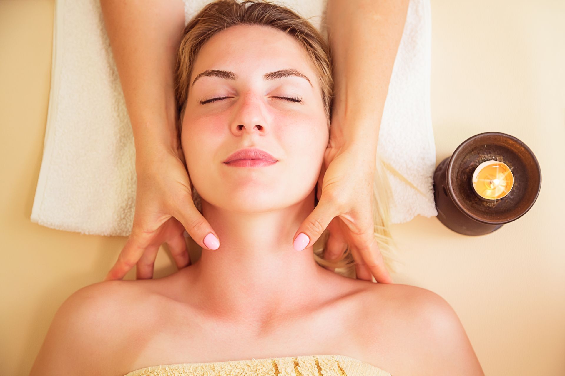 Woman receiving neck massage at a spa, lit candle beside her.
