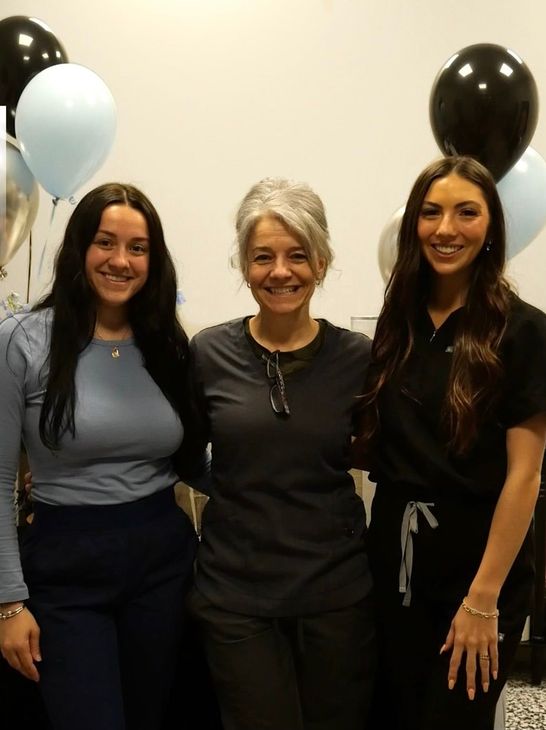 Three women are posing for a picture with balloons in the background.