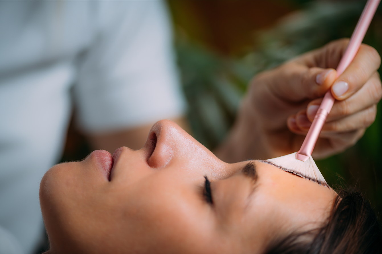 Cosmetic brush applying cream to a woman’s forehead during a facial treatment
