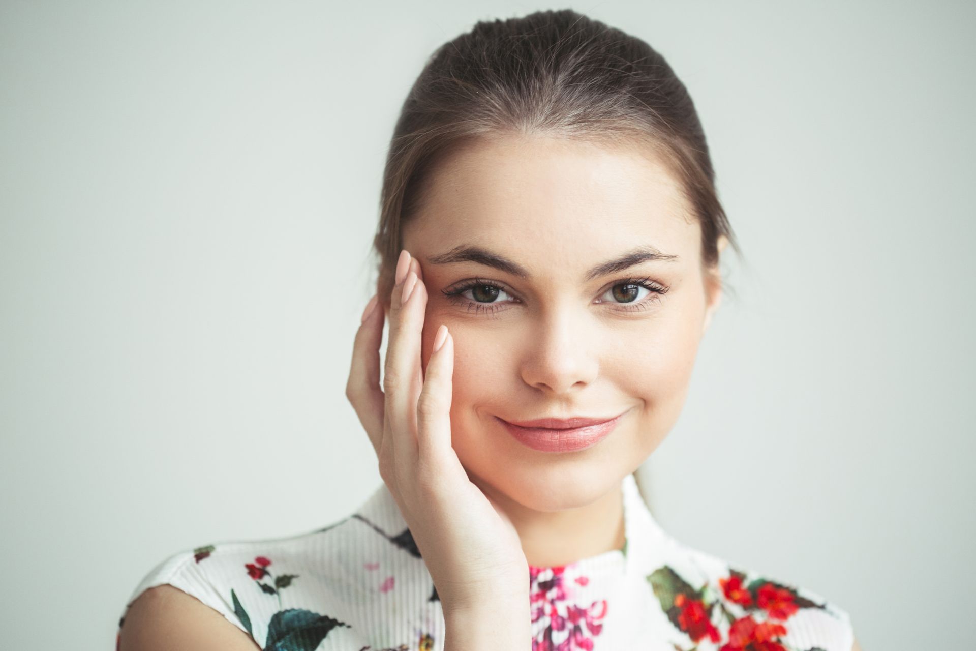 The woman is smiling and touching her face with her hand.