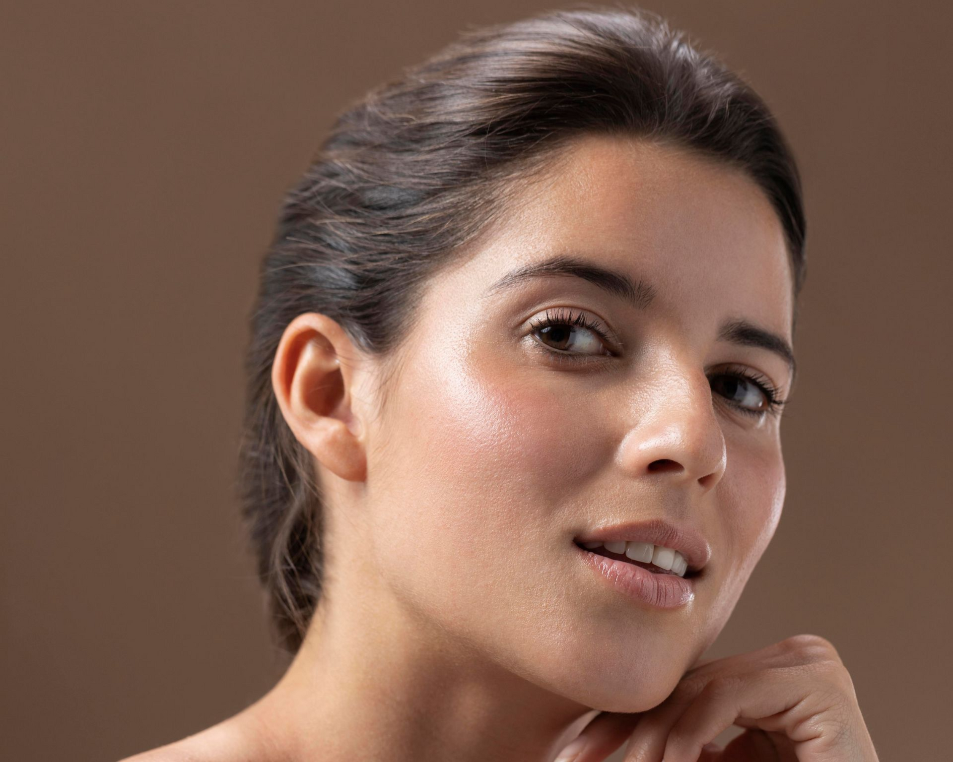 Portrait of a woman with dark hair resting her chin on her hand against a plain brown background
