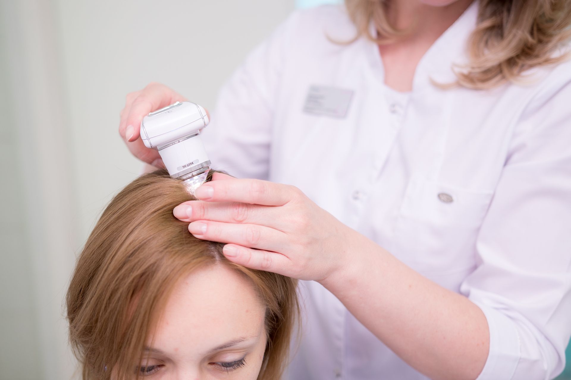 Woman receiving scalp treatment from a healthcare professional, indoors.