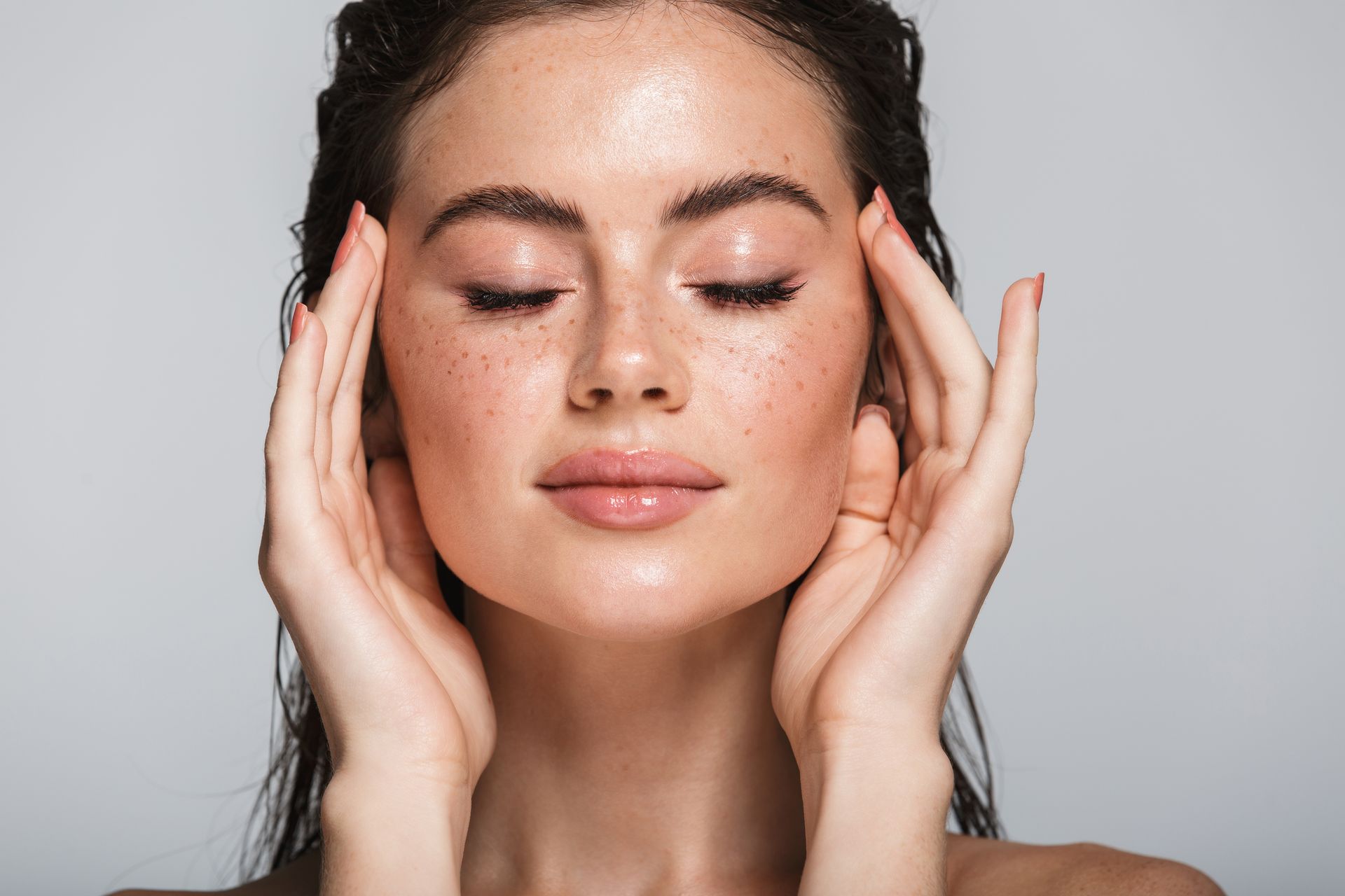 A woman with freckles is touching her face with her hands.