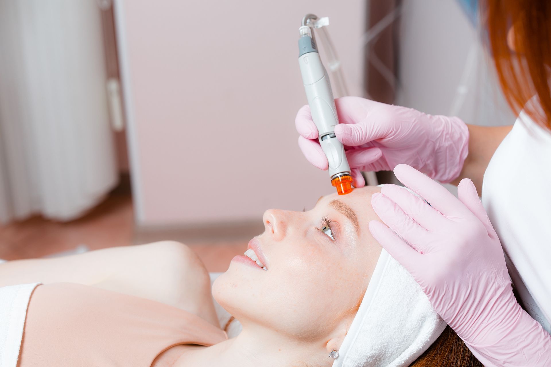 Esthetician performing facial treatment with a handheld device on a reclining client in a spa room