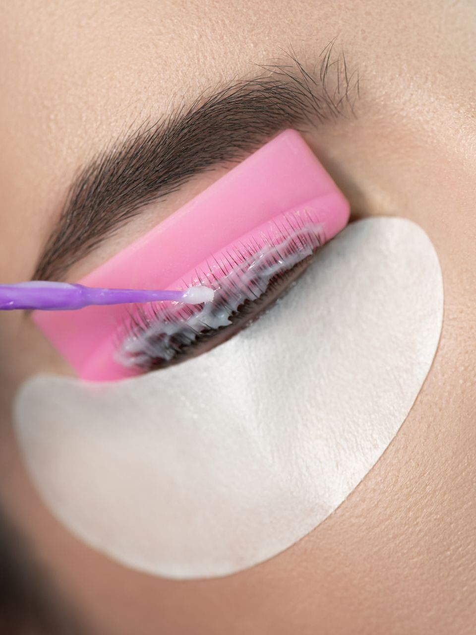 A woman is getting eyelash extensions with a pink brush.