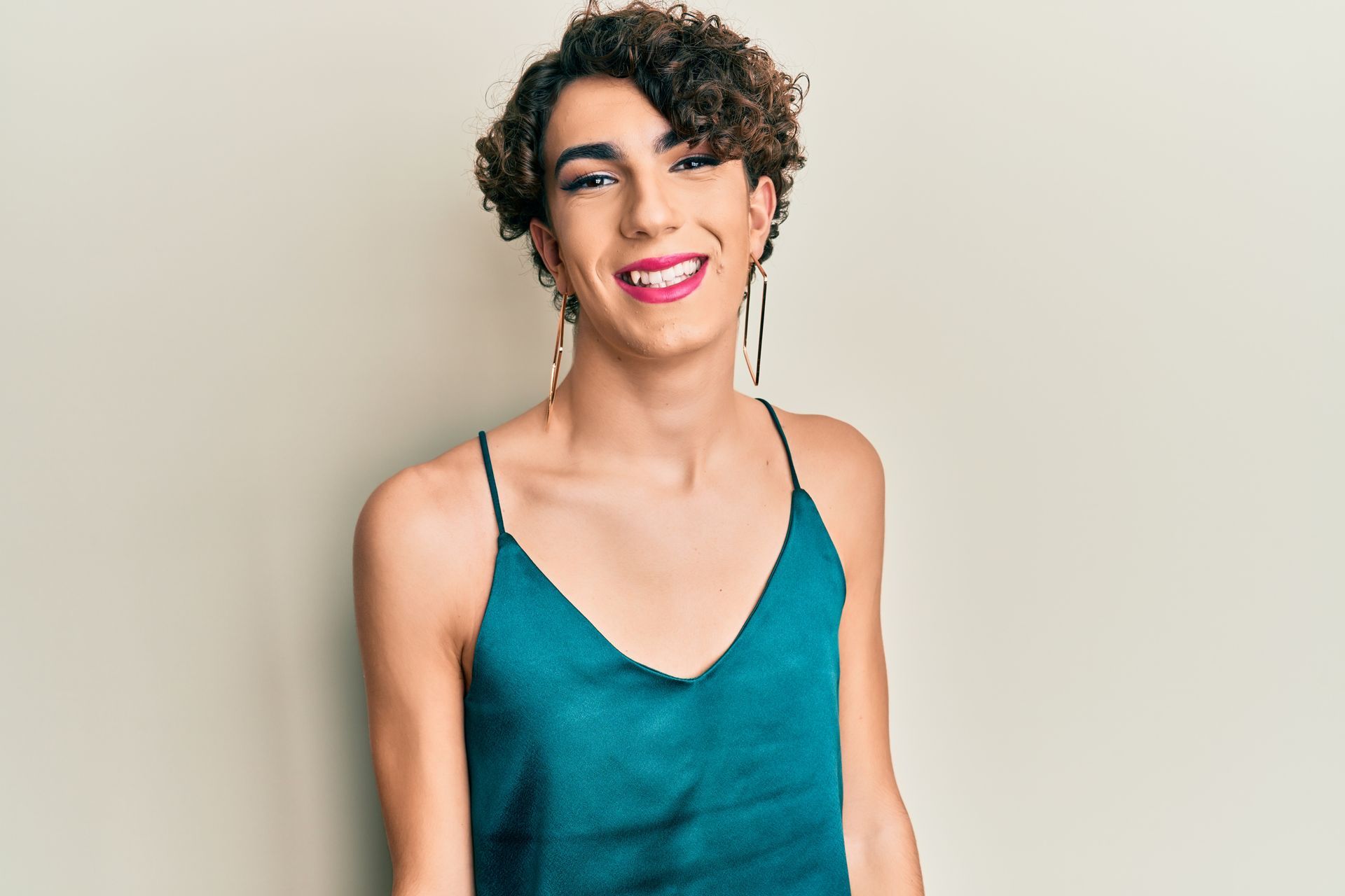 Person smiling, wearing a teal tank top and dangling earrings. Curly hair, neutral background.