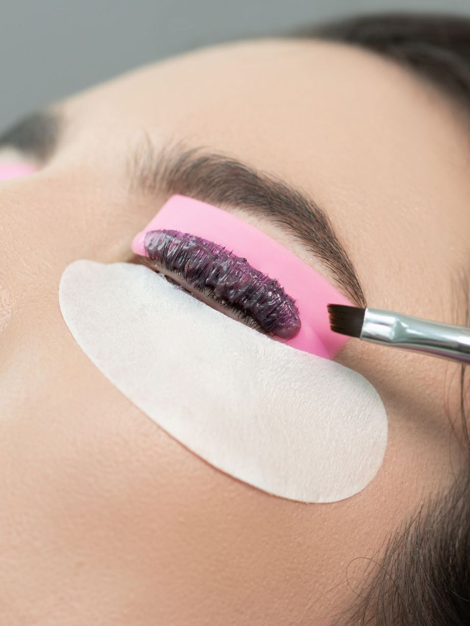 A woman is getting her eyelashes done with a brush.