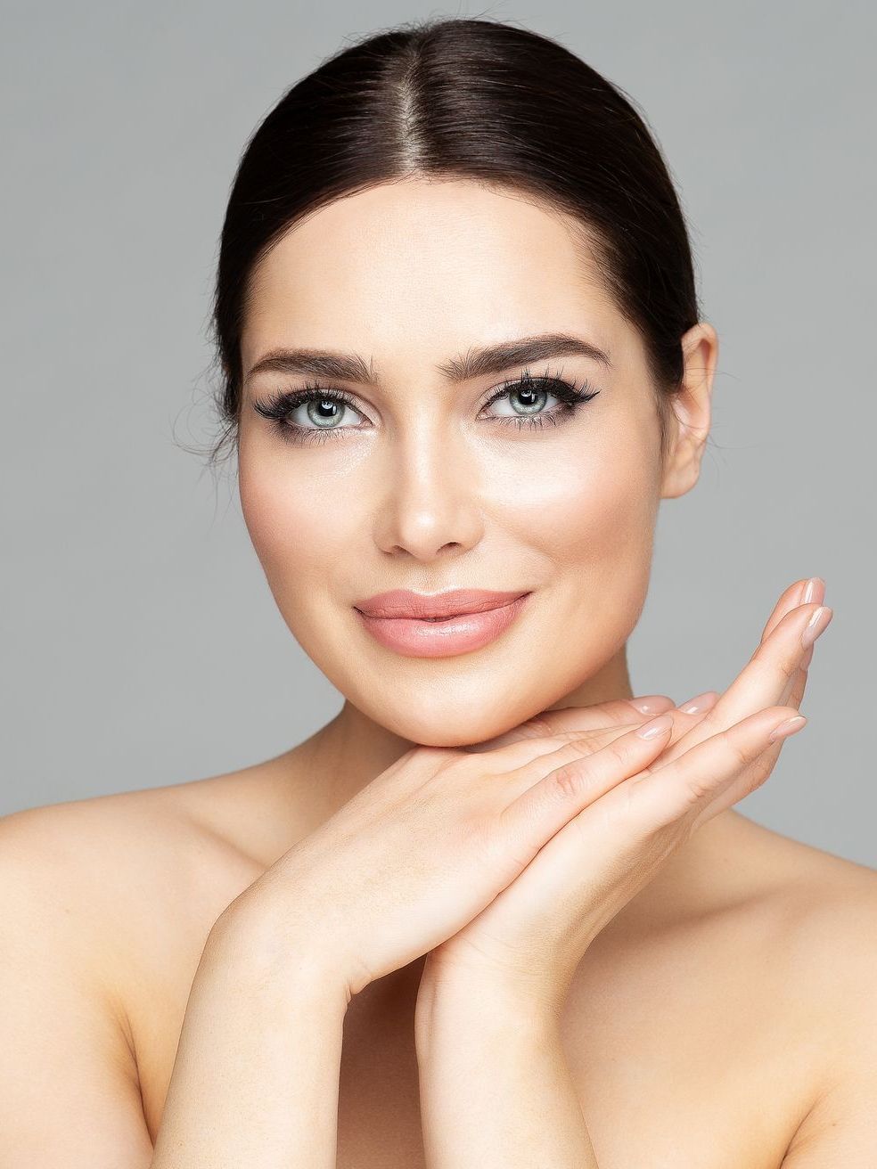 A woman is touching her face with her hands and smiling.